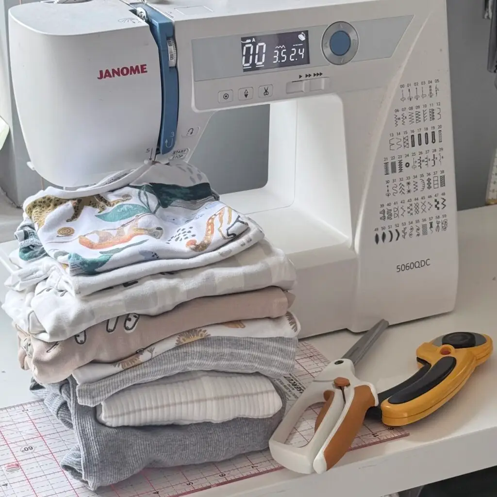 Baby clothes laid nect to a sewing machine ready for a custom memory quilt